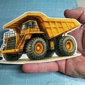 May include: A yellow and brown watercolour illustration of a large dump truck. The truck has large black tyres with yellow rims, a detailed cab, and a large bed. The image is a sticker or cutout.