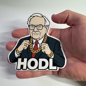 May include: A sticker featuring a cartoon illustration of a man in a suit, glasses, and gold jewelry. The word "HODL" is printed in bold letters at the bottom. The sticker is held in a hand.