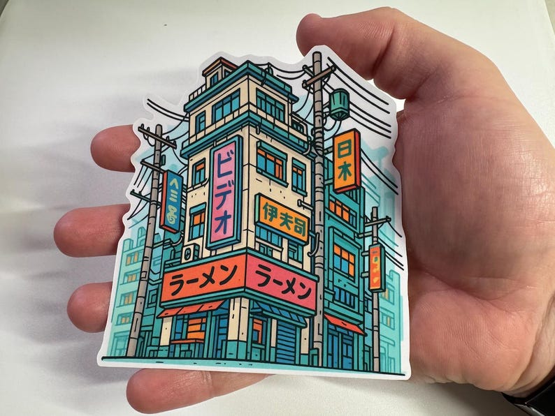 Puede incluir: Una colorida pegatina con una ilustraci&oacute;n estilizada de un restaurante de ramen japon&eacute;s. El edificio de varios pisos tiene letreros en japon&eacute;s. La paleta de colores incluye verde azulado, naranja y rosa.