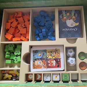 May include: A wooden board game organizer with various game components. Includes orange, blue, and green wooden pieces, cards with illustrations, dice, and tokens. The "Overview" card is visible.