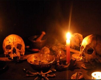 May include: A dark, dimly lit scene with two human skulls, a lit candle, and other occult objects. The skulls are positioned on a dark surface, with the candle casting a warm glow on the scene.