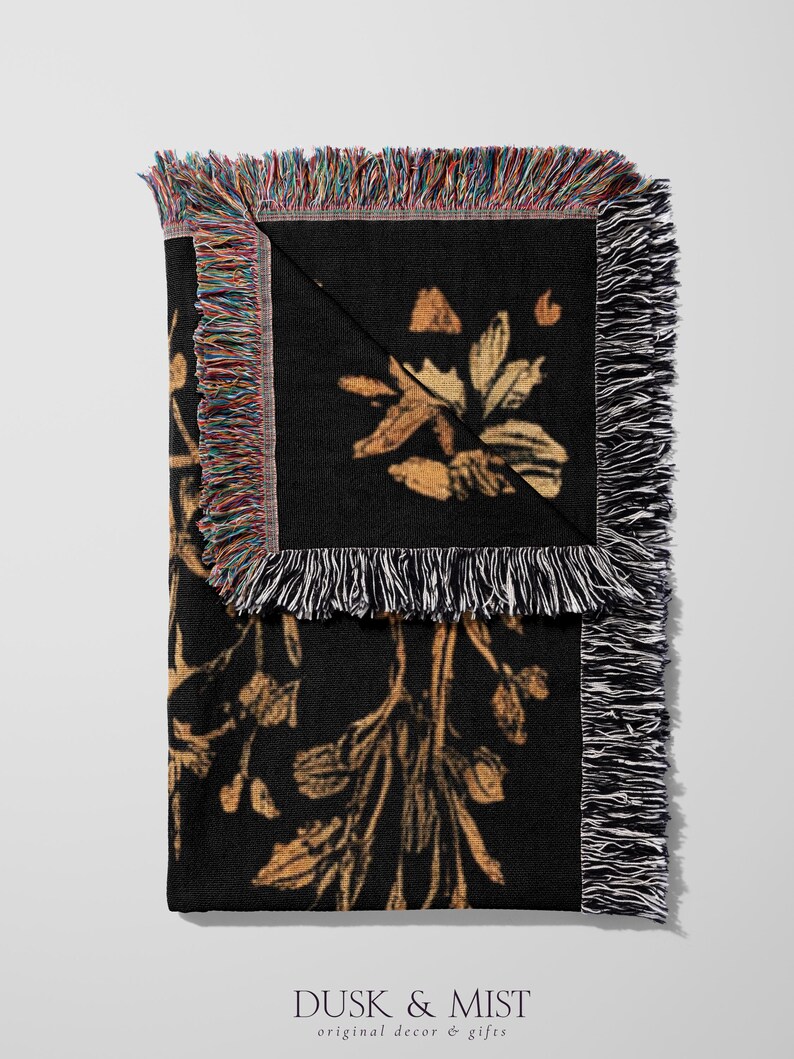 A woven throw blanket showcasing a majestic black dragon curled among mushrooms and botanical foliage beneath a glowing golden moon. The rich fantasy design, filled with forest plants and mystical details, is illustrated in earthy tones of crimson, gold, and deep brown on a dark backdrop.