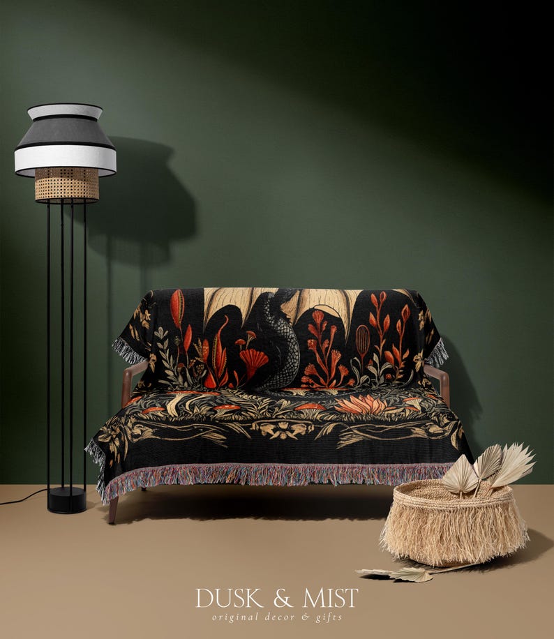 A woven throw blanket showcasing a majestic black dragon curled among mushrooms and botanical foliage beneath a glowing golden moon. The rich fantasy design, filled with forest plants and mystical details, is illustrated in earthy tones of crimson, gold, and deep brown on a dark backdrop.
