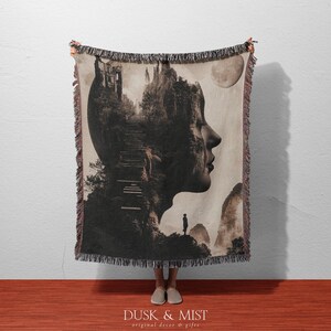 May include: A woven throw blanket featuring a surreal design of a profile with a landscape and stairs inside. The blanket has a fringed edge and a neutral color palette with the text "Dusk & Mist original decor & gifts".