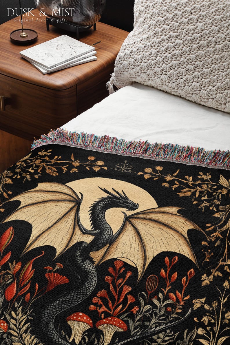 A woven throw blanket showcasing a majestic black dragon curled among mushrooms and botanical foliage beneath a glowing golden moon. The rich fantasy design, filled with forest plants and mystical details, is illustrated in earthy tones of crimson, gold, and deep brown on a dark backdrop.