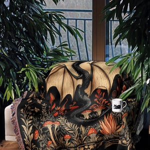 A woven throw blanket showcasing a majestic black dragon curled among mushrooms and botanical foliage beneath a glowing golden moon. The rich fantasy design, filled with forest plants and mystical details, is illustrated in earthy tones of crimson, gold, and deep brown on a dark backdrop.