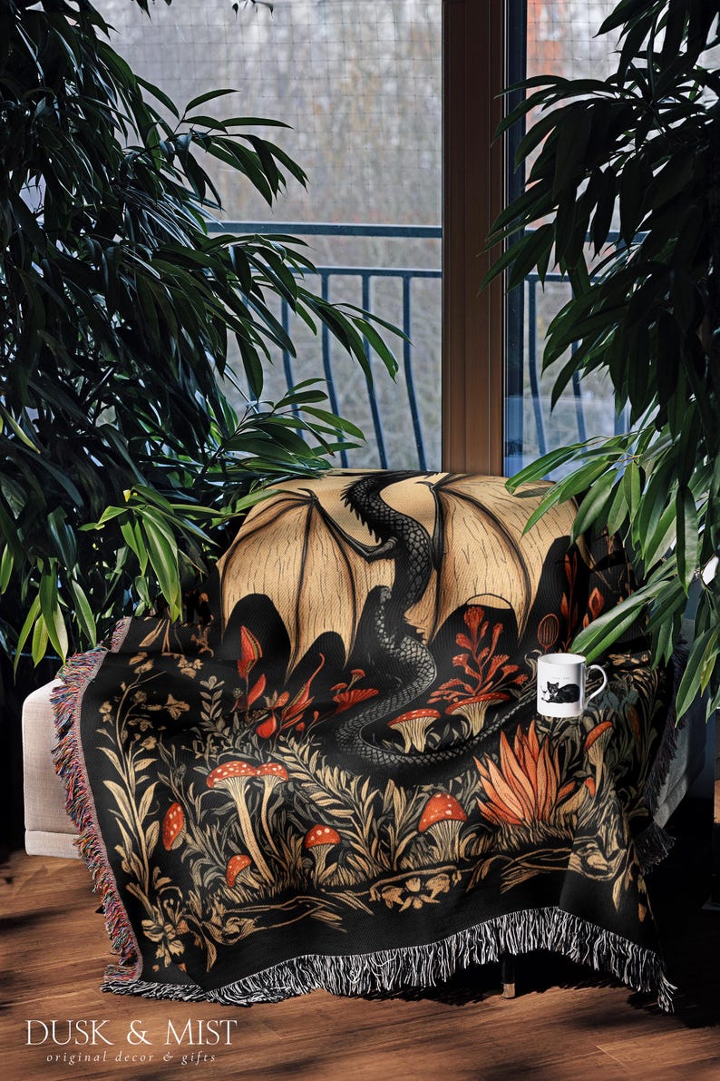 A woven throw blanket showcasing a majestic black dragon curled among mushrooms and botanical foliage beneath a glowing golden moon. The rich fantasy design, filled with forest plants and mystical details, is illustrated in earthy tones of crimson, gold, and deep brown on a dark backdrop.