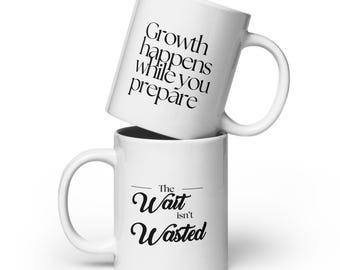 Puede incluir: Dos tazas de cerámica blanca apiladas. La taza superior tiene el texto negro "Growth happens while you prepare". La taza inferior tiene el texto negro "The Wait isn't Wasted".