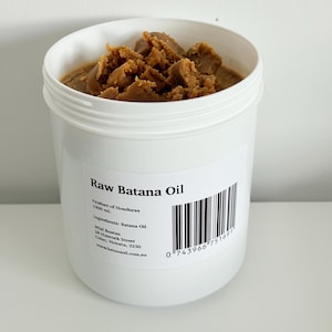 Peut inclure: Un récipient en plastique blanc contenant de l'huile de Batana brute. L'étiquette indique "Raw Batana Oil" et comprend un code-barres. L'huile est brun clair et a une texture. Le produit, originaire du Honduras, contient 1000 ml.