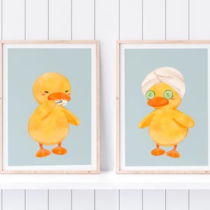 May include: Two framed illustrations of a yellow duck. One duck is brushing its teeth and the other duck is wearing a white towel and cucumber slices on its eyes.