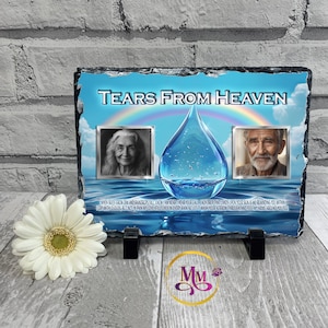 May include: A memorial plaque with the text "Tears From Heaven" above a large water droplet graphic. Two framed portraits flank the droplet. A rainbow and ocean scene are in the background. The plaque is supported by two black stands.