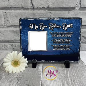Peut inclure: Plaque photo rectangulaire en ardoise avec le texte "My Son Shines Still" et un poème. Le fond est une scène de nuit étoilée. Une fleur blanche est au premier plan. La plaque est soutenue par deux supports noirs.