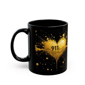 May include: Black ceramic coffee mug with a gold heart design and the text "911 Dispatcher" inside the heart. The heart is surrounded by gold splatters on a black background.