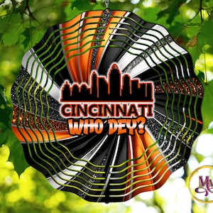 Pode incluir: Um moinho de vento preto, branco e laranja com uma silhueta do horizonte de Cincinnati e o texto "Cincinnati Who Dey?" O moinho de vento tem um design em espiral com detalhes de glitter.