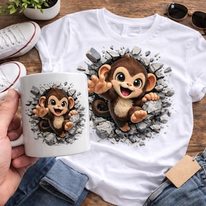 以下が含まれることがあります： 白いTシャツとマグカップに漫画の猿のデザイン。猿は灰色の石の壁を突き破っているように見えます。猿は茶色で、お腹はベージュで、口を開けて笑っています。