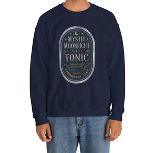 May include: A navy blue sweatshirt with a vintage-style label that reads "Mystic Moonlight Tonic" with a crescent moon and stars. The label also says "Infused with Lunar Magic" and "Apothecary Tonic".