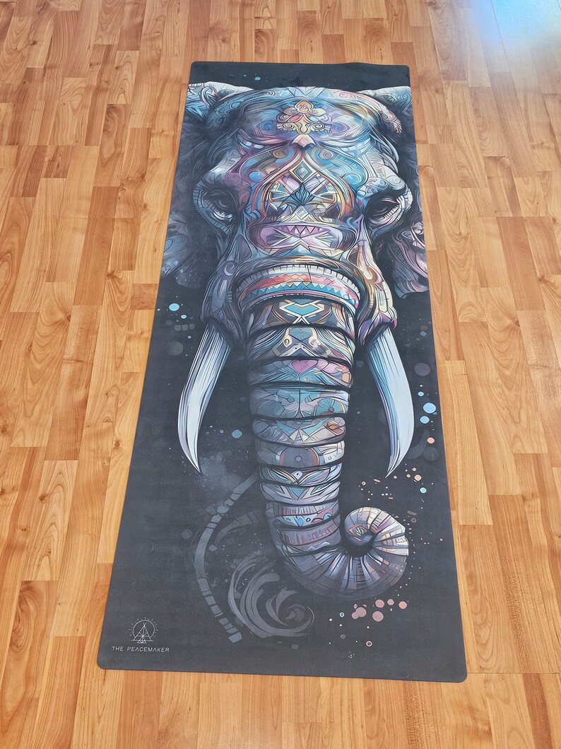 May include: A yoga mat with a colorful, detailed illustration of an elephant's face. The elephant's trunk is curled up and the background is black with white speckles. The text "THE PEACEMAKER" is at the bottom of the mat.