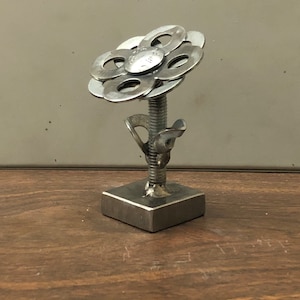 May include: A silver metal flower sculpture made from washers and a bolt. The flower has six petals and is mounted on a square base.