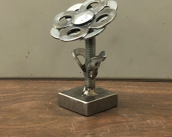 May include: A silver metal flower sculpture made from washers and a bolt. The flower has six petals and is mounted on a square base.