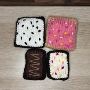 Puede incluir: Cuatro posavasos tejidos con temática de comida. Un posavasos blanco con manchas negras, un posavasos rosa con chispas, un posavasos marrón con un diseño ondulado marrón y un posavasos blanco con chispas naranjas, amarillas y rojas. Todos tienen bordes marrones oscuros.