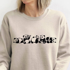 May include: A beige sweatshirt with a black graphic of five pandas. The pandas are in various poses, including sleeping, playing, and eating bamboo.