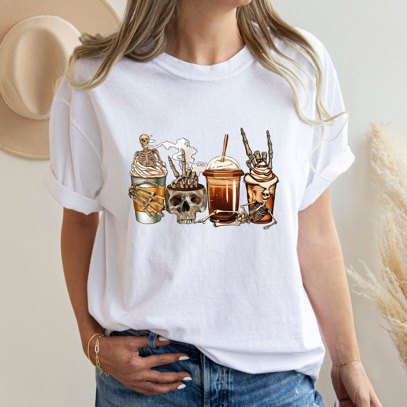 May include: White t-shirt with a graphic of skeletons drinking coffee and iced coffee. The skeletons are wearing hats and sunglasses.