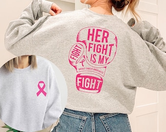 May include: Gray sweatshirt with a pink boxing glove graphic that says "Her Fight Is My Fight" and "Breast Cancer Awareness".