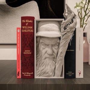 May include: A still-life arrangement featuring books and decorative items. The books include "The Works of William Shakspere" and "The Man Who Was Thursday". A bust of a man with a long beard is in a frame. A carved wooden piece and a vase with flowers are also present.