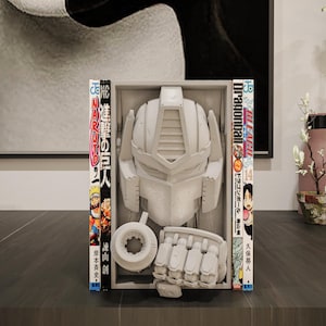 May include: A gray, detailed model of a robot's head, hand, and other parts, displayed in a box. The box is flanked by Japanese manga books, including "Naruto" and "Dragonball". The items are on a dark surface, with a neutral background.