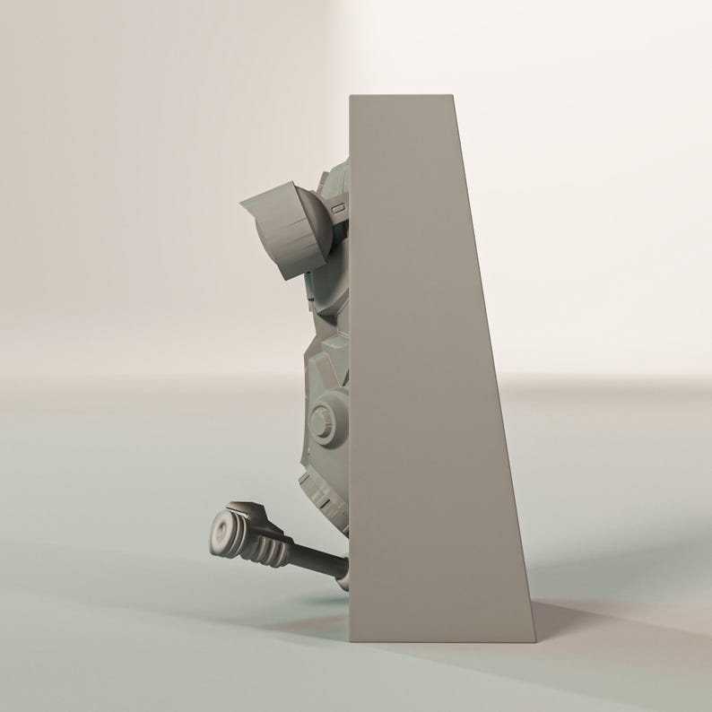 May include: A gray, three-dimensional model of a mechanical object, possibly a robot or part of a larger machine. The model has a complex design with various geometric shapes, cylinders, and circular elements. The object is partially obscured by a gray rectangular structure.