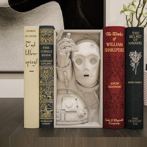 以下が含まれることがあります： 白いC-3POの胸像と、ヴィンテージの本が並んだ装飾的な本棚の配置。本には「ジャングルブック」や「ウィリアム・シェイクスピアの作品」などのタイトルがあります。白い花が入った花瓶やその他の装飾品がディスプレイを完成させています。