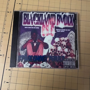May include: A CD case with a black and purple design. The title of the album is "BLVCKL VND RVDIX" and the text "SUCK A DICK FOR 2011 SWAG" is printed on the front. The album cover features a person wearing a pink shirt and a skull necklace. The text "DOPEST ALBUM IN 1991" is printed on the front of the case. The text "MONEY JORDAN" is printed below the text "DOPEST ALBUM IN 1991". The text "PARENTAL ADVISORY EXPLICIT CONTENT" is printed on the right side of the case.
