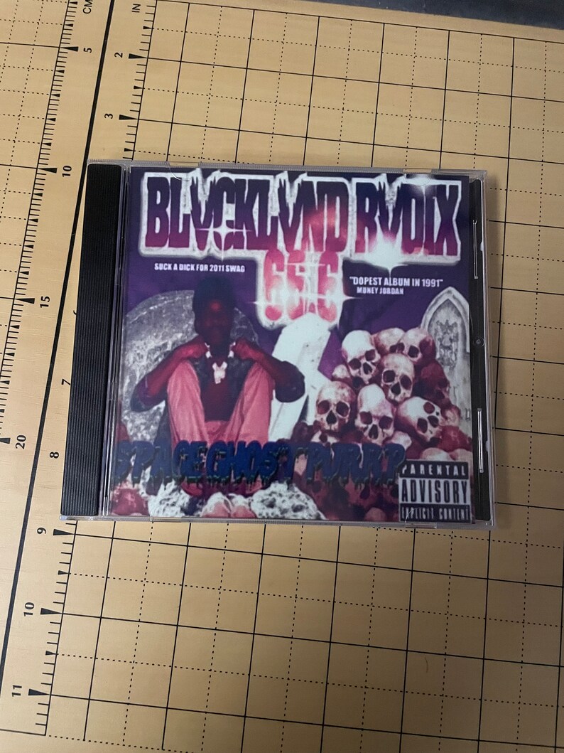 May include: A CD case with a black and purple design. The title of the album is "BLVCKL VND RVDIX" and the text "SUCK A DICK FOR 2011 SWAG" is printed on the front. The album cover features a person wearing a pink shirt and a skull necklace. The text "DOPEST ALBUM IN 1991" is printed on the front of the case. The text "MONEY JORDAN" is printed below the text "DOPEST ALBUM IN 1991". The text "PARENTAL ADVISORY EXPLICIT CONTENT" is printed on the right side of the case.