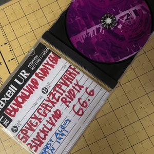 May include: A black CD case with a purple CD inside. The case has handwritten text on it, including "BLVCKLVND RUDIX", "SPVCX CAXZTPVRRF", "POPEST ALBUM", "IN 1991", and "66.6".