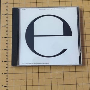 May include: A square CD jewel case with a white cover featuring a large black lowercase letter e. The top edge displays track titles including AAA Powerline, Peroxide, and Fragile. The bottom edge lists tracks like Calcium, Sugar & Diesel, and Blue Eyes.