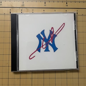May include: A white CD case with a blue and red New York Yankees logo and a red signature. The case is in a black jewel case.