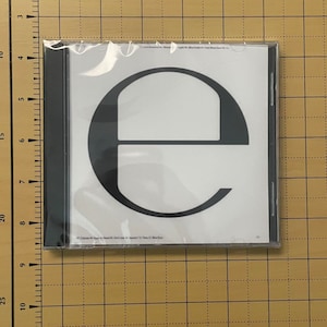 May include: A white CD case with a black letter 'e' printed on the front. The CD case is in a plastic sleeve.