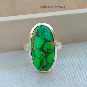May include: A silver ring with a green oval turquoise stone. The stone has a marbled pattern with gold flecks.