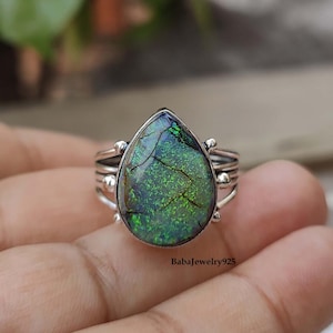 May include: A silver ring with a teardrop-shaped green opal gemstone. The ring has a delicate design with small beads around the stone.