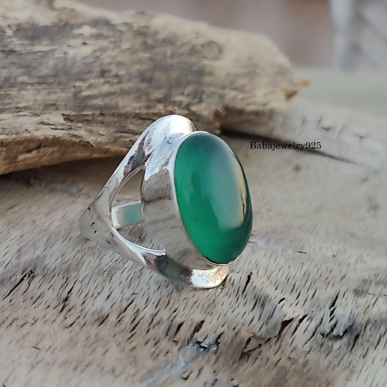 May include: A silver ring with a green oval gemstone set in a unique, open design. The ring is on a wooden surface.