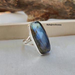 May include: A silver ring featuring a large, rectangular, iridescent labradorite gemstone. The stone displays a blue, green, and black colour.
