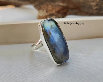 Può includere: Un anello d'argento con una grande pietra rettangolare di labradorite iridescente. La pietra è di colore blu, verde e nero.