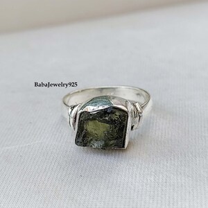 May include: A silver ring with a green gemstone. The ring has a twisted band and the gemstone is a rough cut.