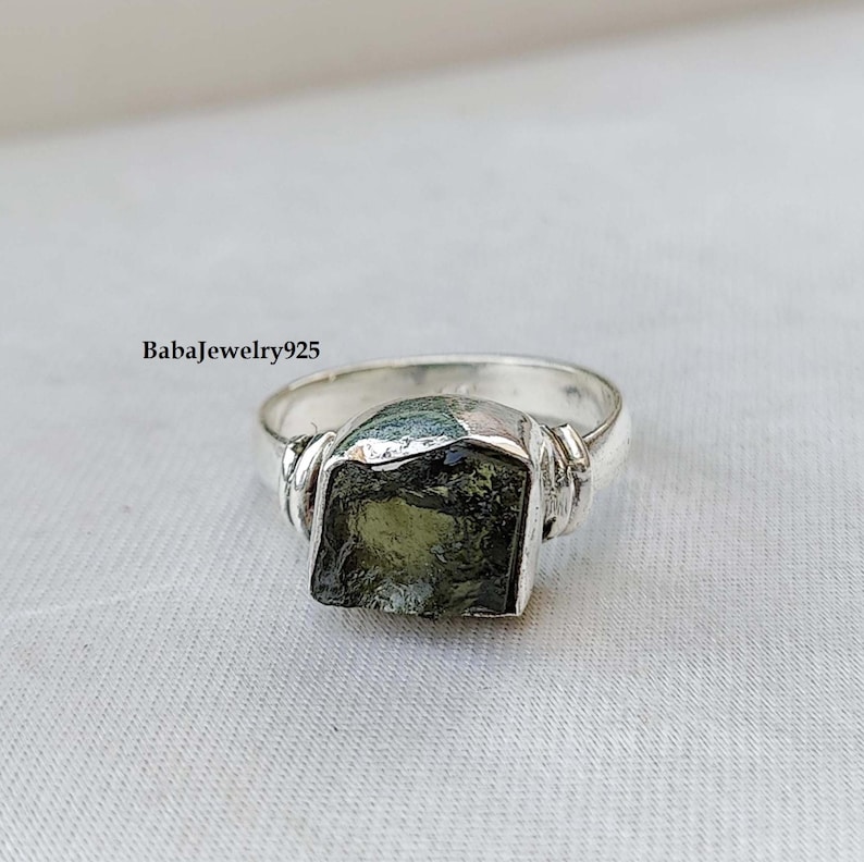 May include: A silver ring with a green gemstone. The ring has a twisted band and the gemstone is a rough cut.