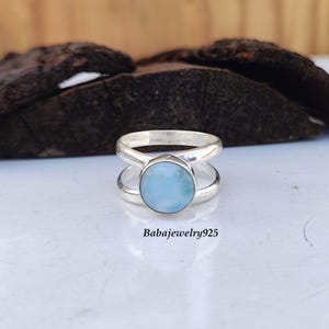 Könnte beinhalten: Ein silberner Ring mit einem hellblauen Edelstein. Der Ring hat ein Doppelband-Design.