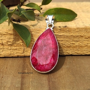 May include: A teardrop-shaped pendant with a red gemstone set in sterling silver. The pendant is on a wooden surface.