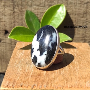 May include: A silver ring with a black and white oval gemstone. The ring is on a wooden surface.