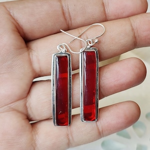 May include: A pair of silver dangle earrings with red rectangular gemstones.