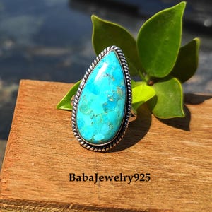 May include: A turquoise gemstone ring with a teardrop-shaped stone set in a silver band. The ring has a rope-like design around the edge of the setting.