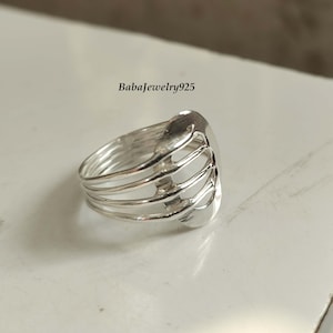 May include: A silver ring featuring a distinctive openwork design. The ring has a wide band and a geometric pattern that resembles a cage or a grid.